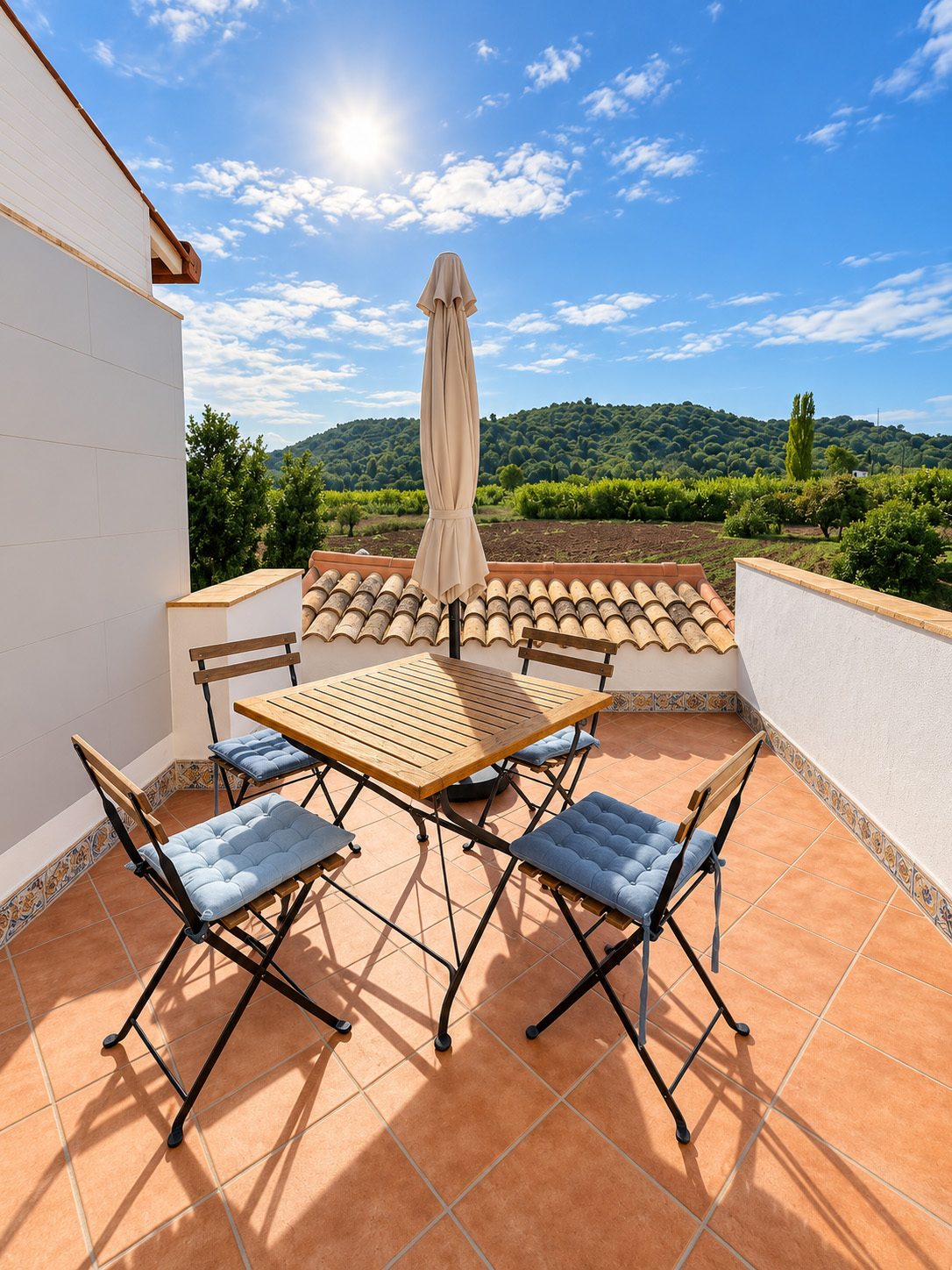 Terrasse mit Tisch, Stühlen und Sonnenschirm, dahinter Hügel